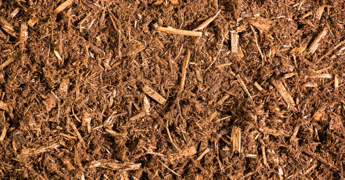 A close-up view of reddish cedar mulch and wood chips spread across the ground in an uneven textured layer.