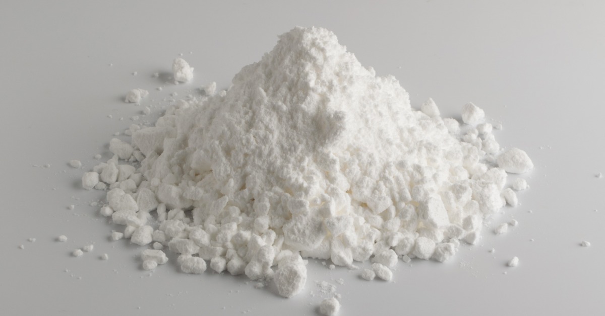 A mound of white powder and small chunks scattered across a smooth gray surface with soft shadows around it.